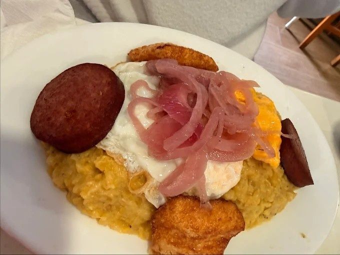 Plato de mofongo cubierto con huevo frito, cebollas encurtidas y salchicha; incluye chips de plátano frito.