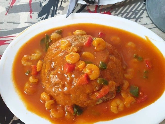 Plato de comida: una cúpula de comida guisada rodeada de una salsa naranja vibrante con camarones, pimientos rojos y verdes.