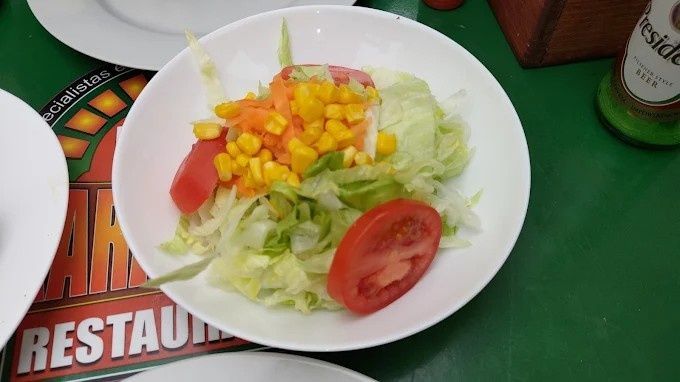 Ensalada con maíz y tomates en un recipiente blanco, sobre una mesa verde con un mantel de restaurante.