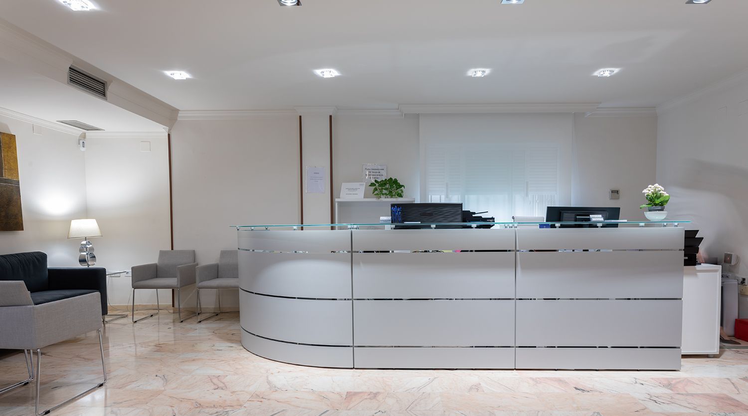 Un área de recepción en un hospital con un mostrador blanco y sillas.