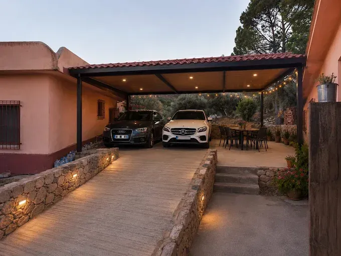 Entrada cubierta con dos coches aparcados junto a una casa color melocotón al atardecer.
