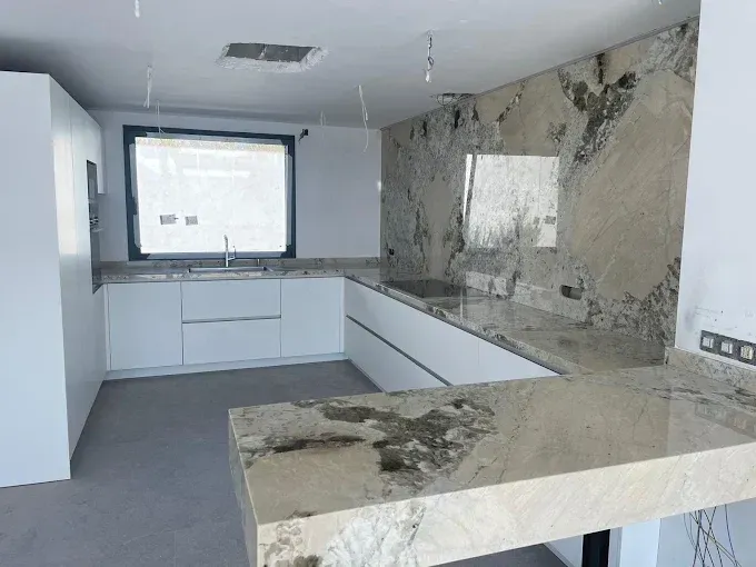 Cocina moderna sin terminar con gabinetes blancos, piso gris y paredes y encimeras de piedra con apariencia de mármol.