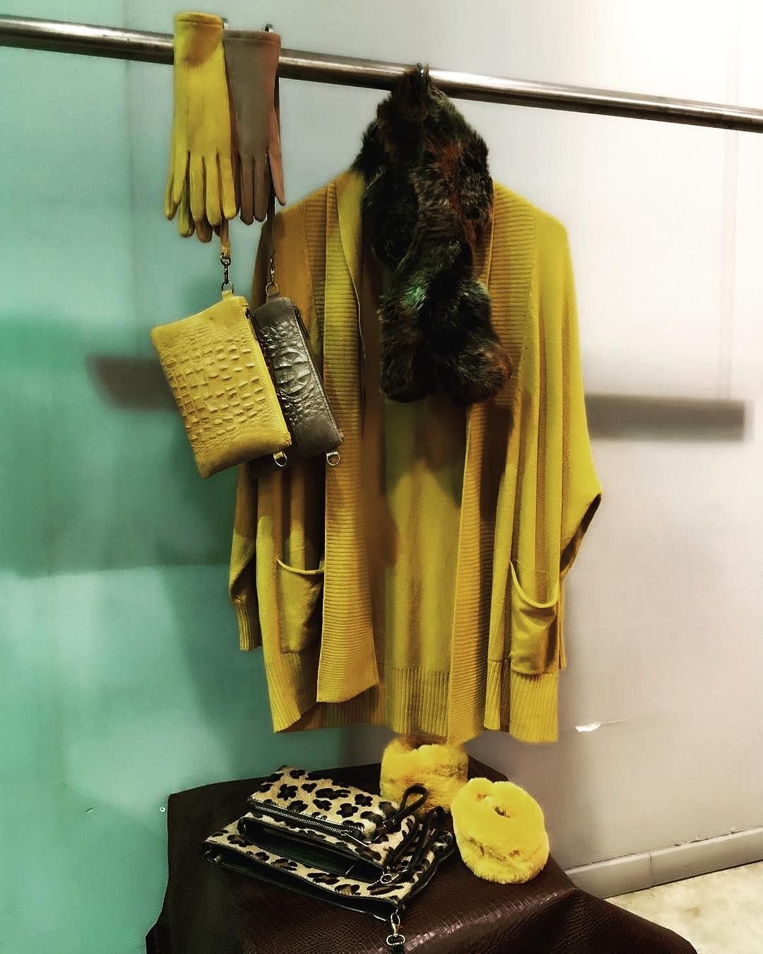 Un cárdigan color mostaza cuelga de un perchero, y debajo se exhiben guantes a juego, una bufanda de piel y bolsos de mano con estampado animal.