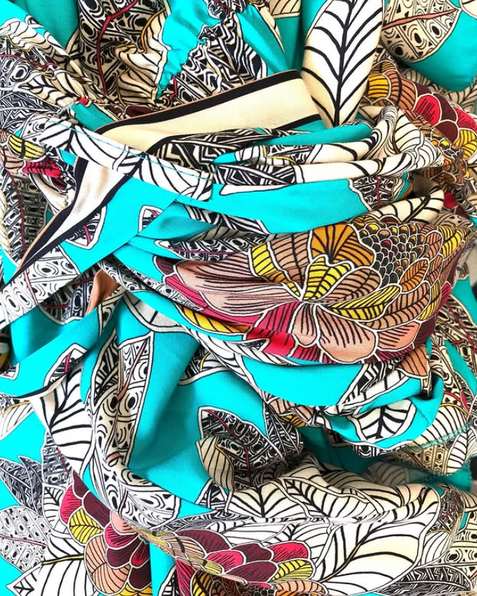Un tejido estampado con hojas estilizadas y motivos florales en vibrantes colores turquesa, negro, blanco, amarillo y rojo.