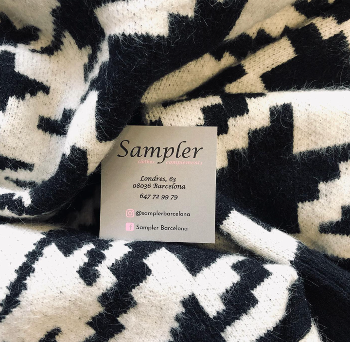 Una tarjeta de visita de Sampler reposa sobre una tela de punto con estampado de pata de gallo en blanco y negro.