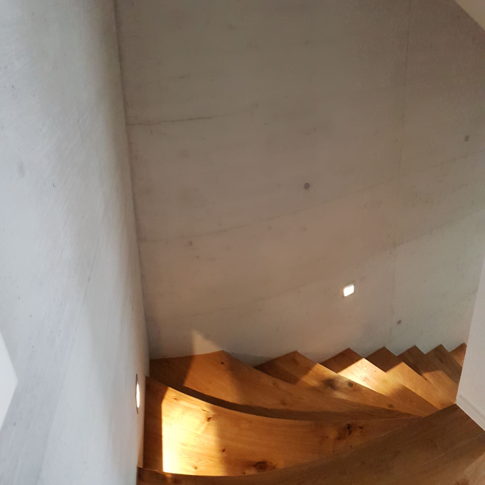 Von oben herab nach unten führende Holztreppe; die Wände sind weiß mit kleinen eingelassenen Lichtern.
