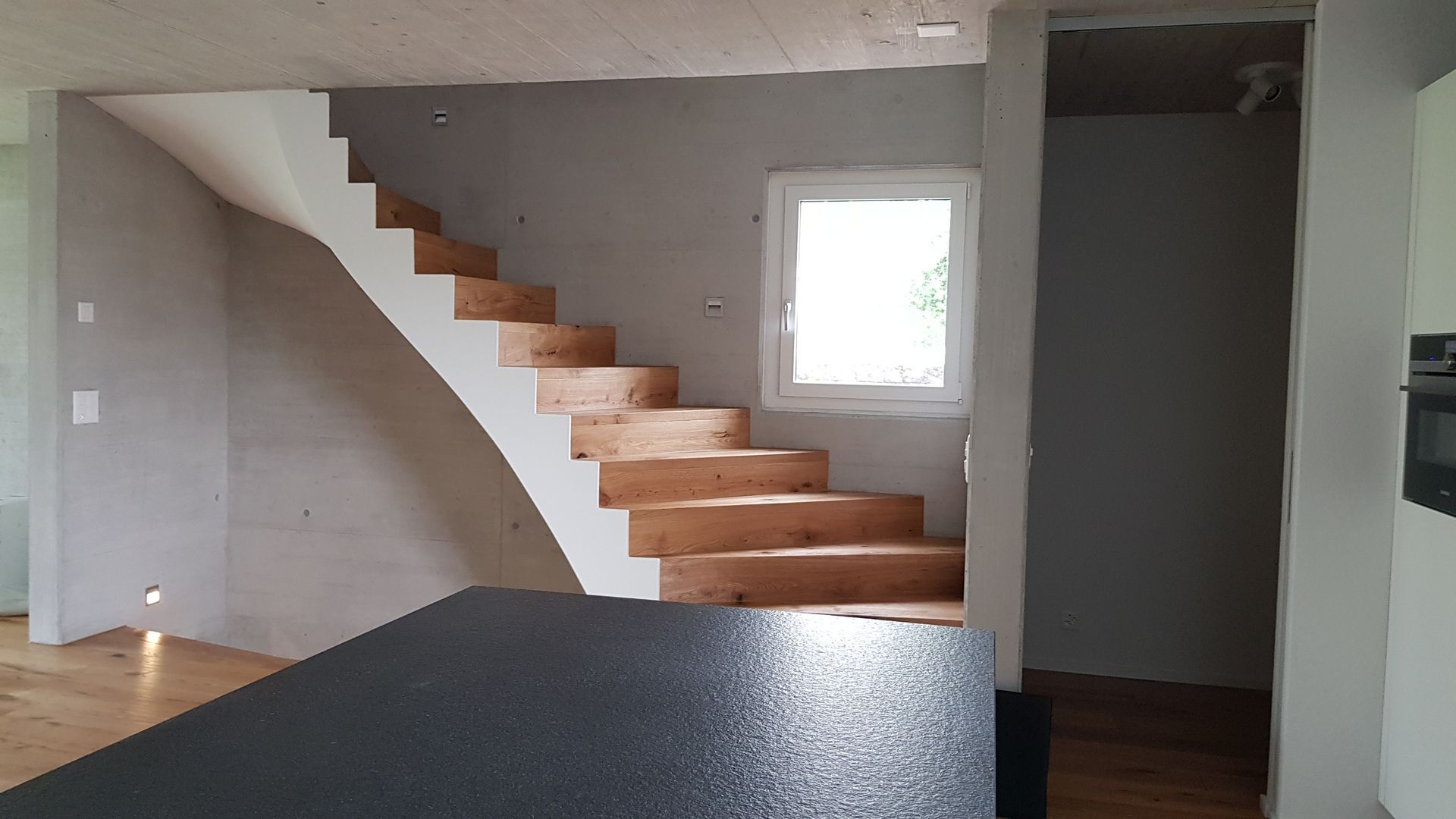 Innenraum mit Holztreppe, kleinem Fenster und unfertigen Wänden.