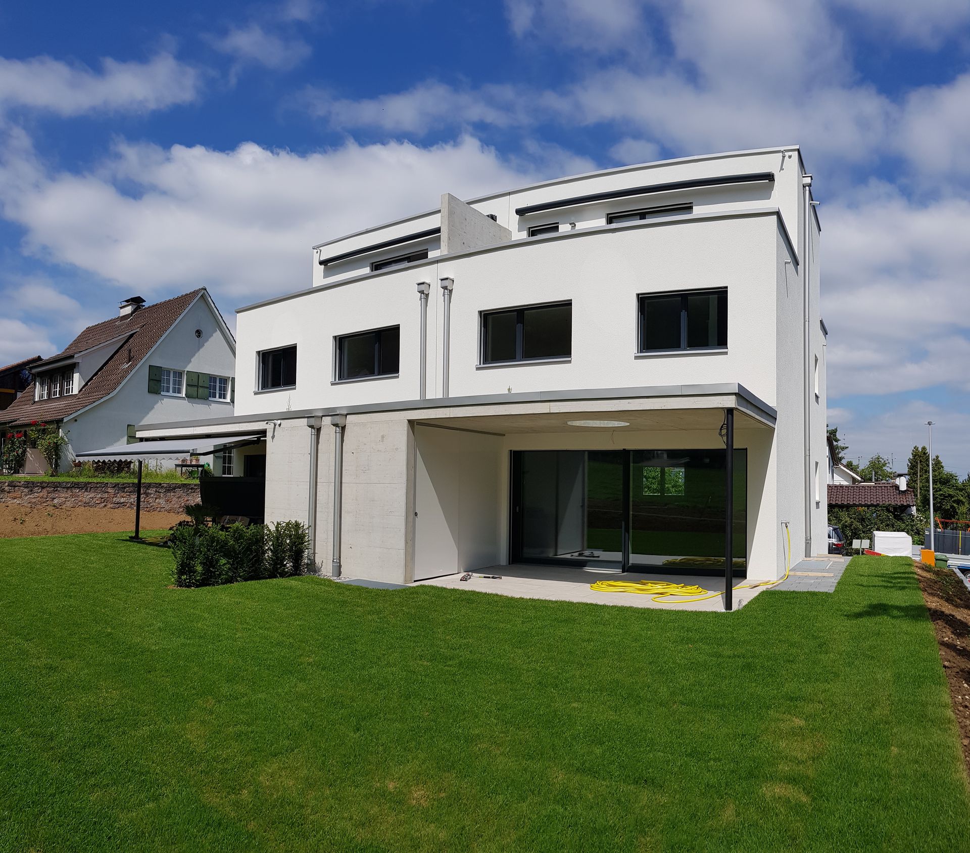 Weißes, modernes Haus mit großen Fenstern, grünem Rasen und blauem Himmel.