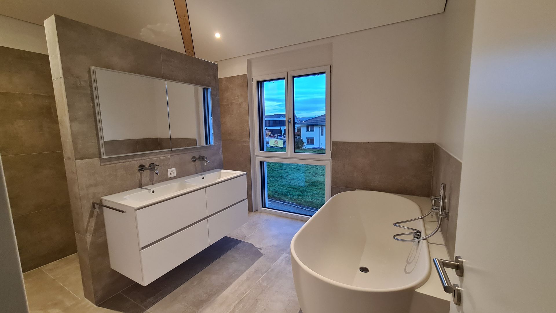 Modernes Badezimmer mit weißer Badewanne, Doppelwaschtisch und großem Fenster.