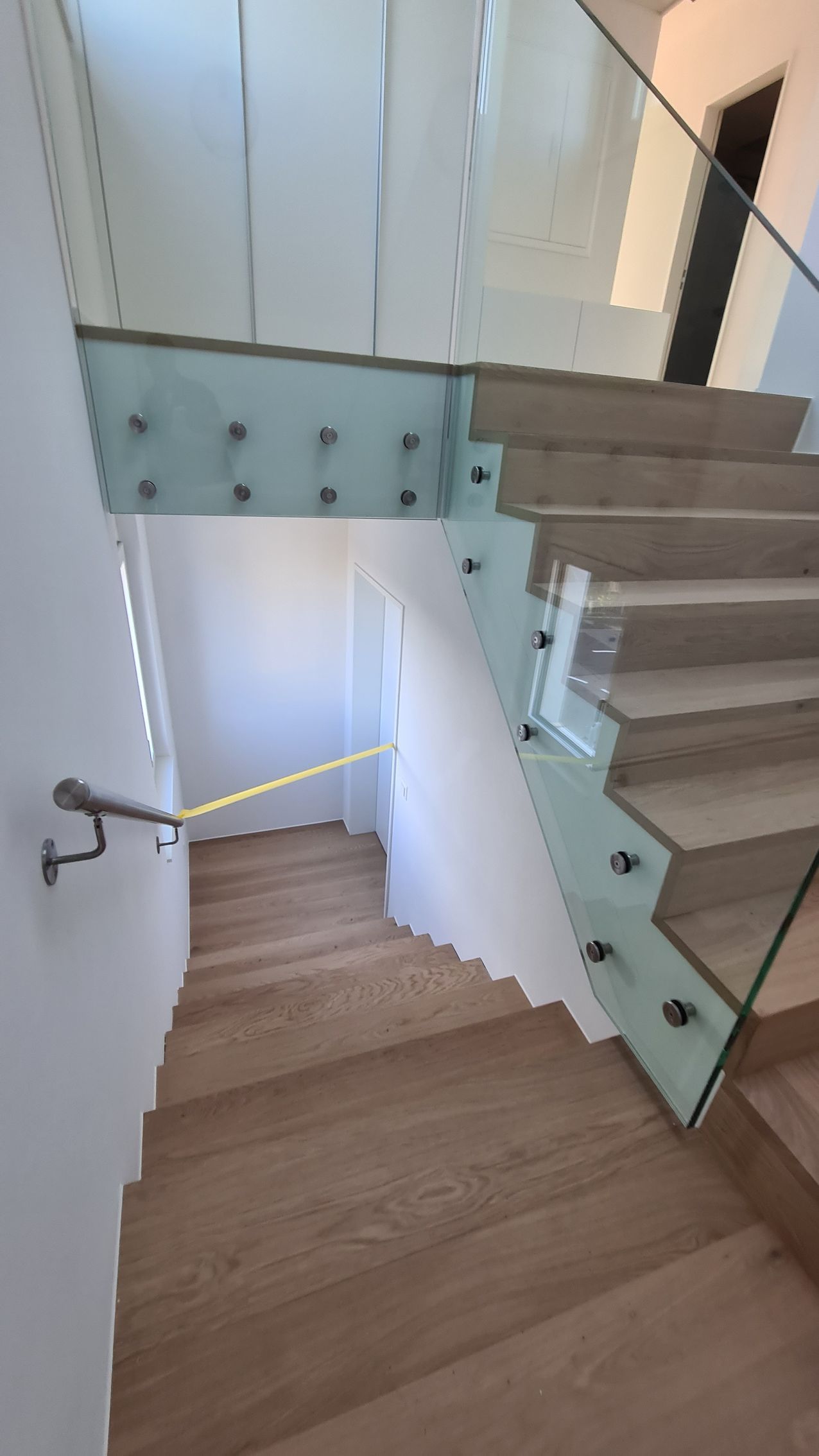Treppe mit Glasgeländer und Holzstufen. Ansicht von oben.