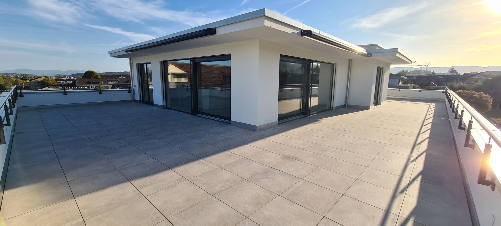 Dachterrasse mit modernem Gebäude, Fliesenboden und malerischer Aussicht unter blauem Himmel.