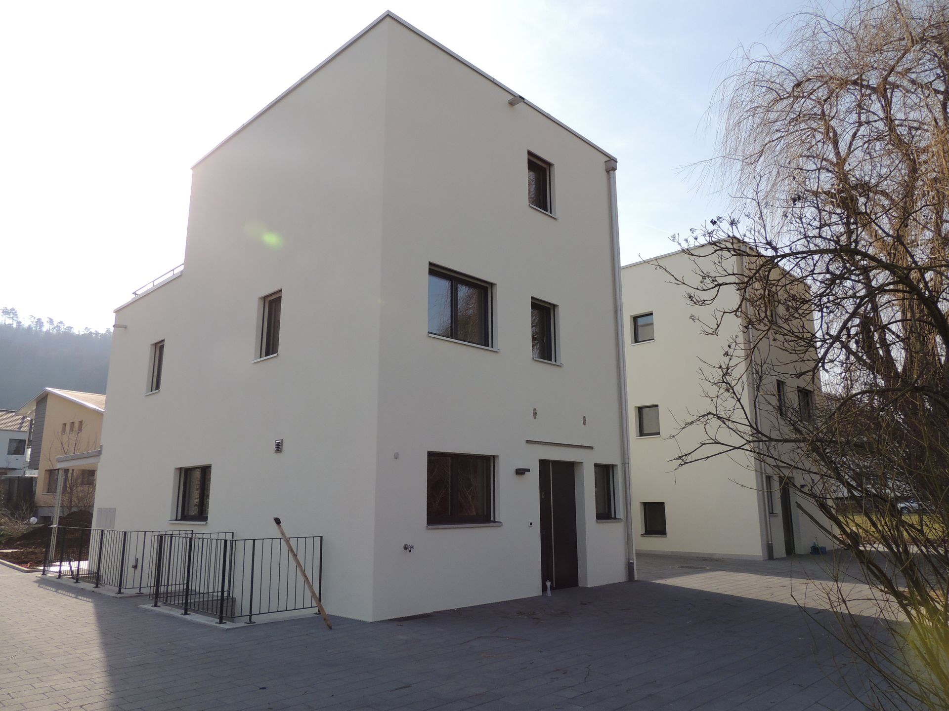 Zwei moderne weiße Gebäude mit dunklen Fenstern und Türen in sonniger Außenumgebung.