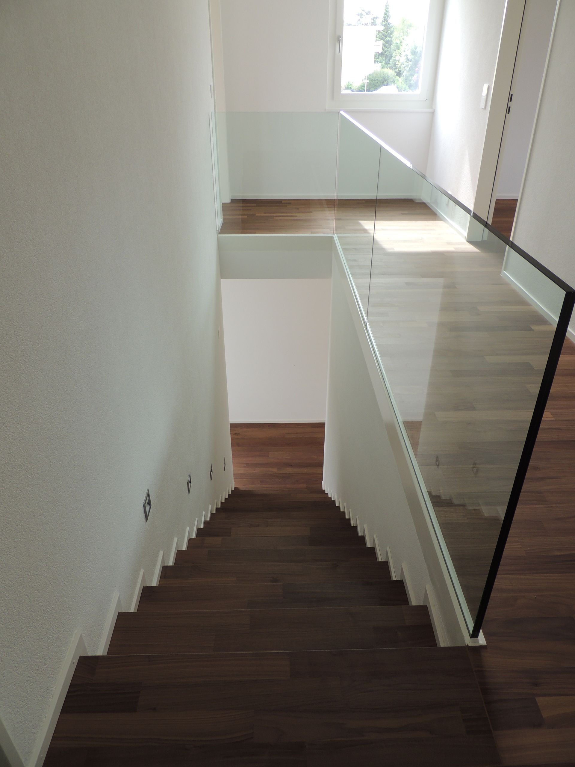Treppe mit Holzstufen und Glasgeländer; weiße Wände; Sonnenlicht durch das Fenster.