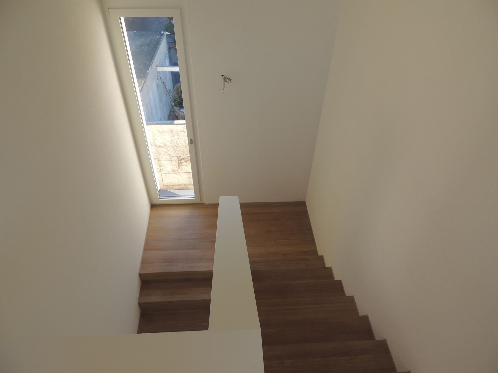 Treppe mit Holzstufen, weißen Wänden und einer Tür mit Sonnenlicht oben.
