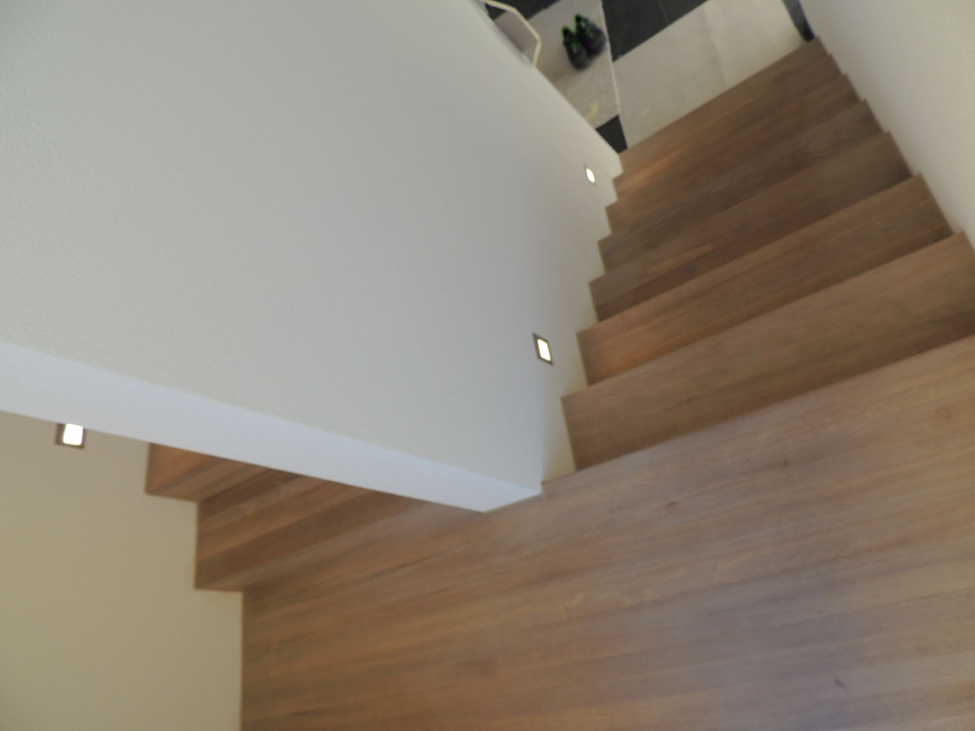 Eine Holztreppe mit Beleuchtung führt von einer weißen Wand nach oben.