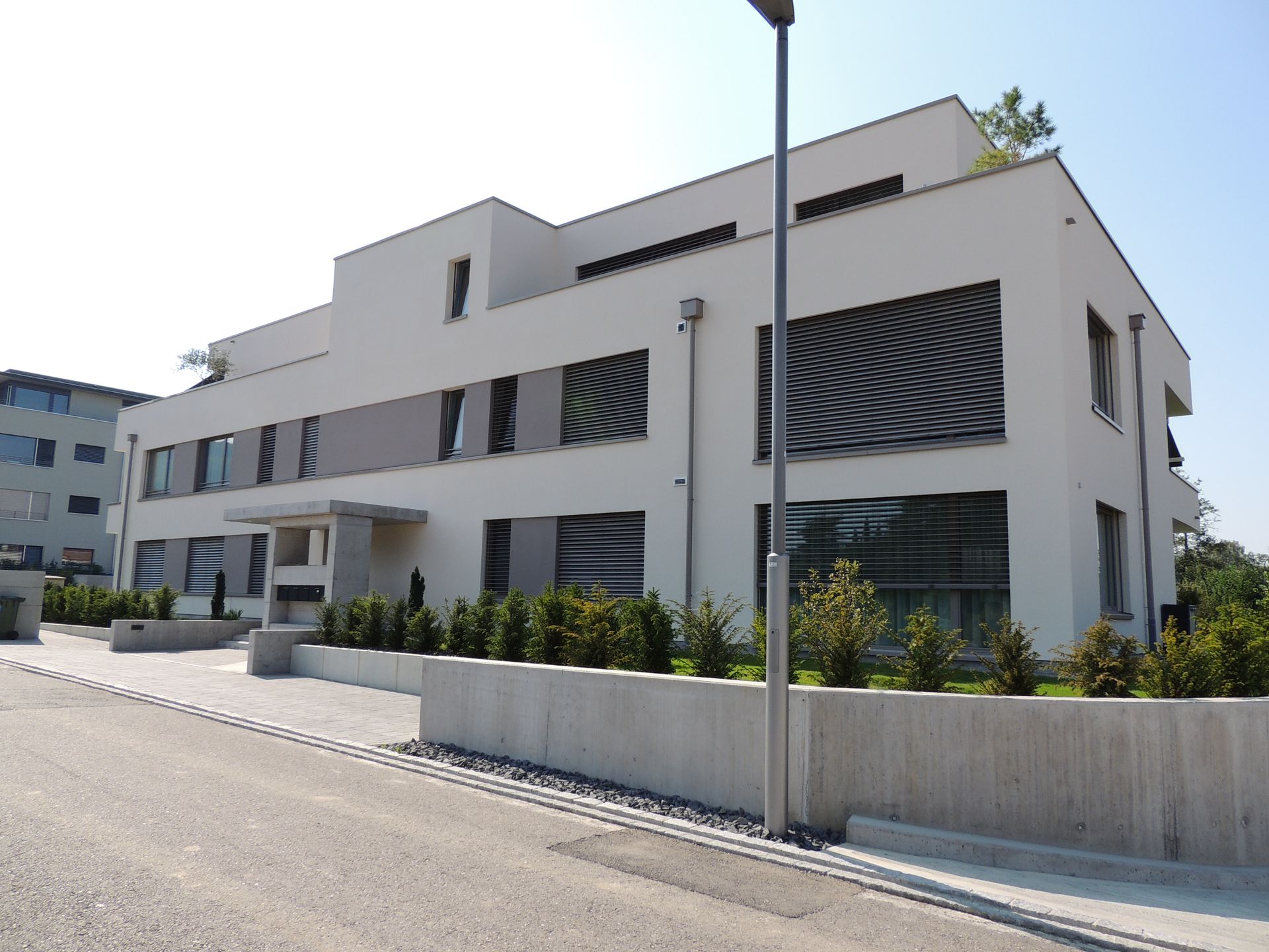 Weißes modernes Gebäude mit großen Fenstern, einem Flachdach und einer Betonwand davor.