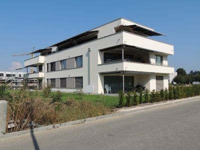 Modernes weißes Mehrfamilienhaus mit Balkonen, sonniger Tag.