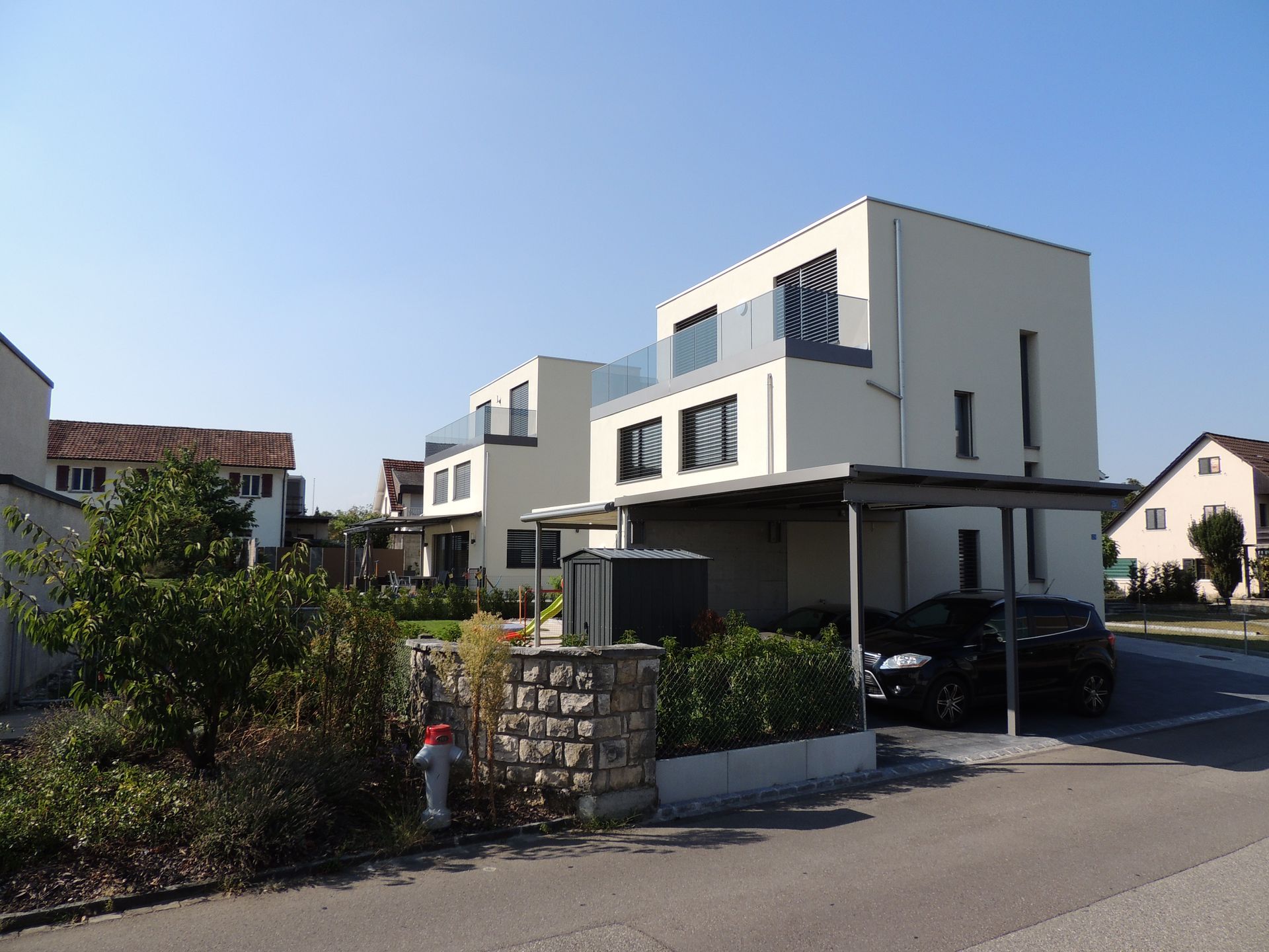 Moderne weiße Stadthäuser mit Balkonen und Carport in einer sonnigen Straße.