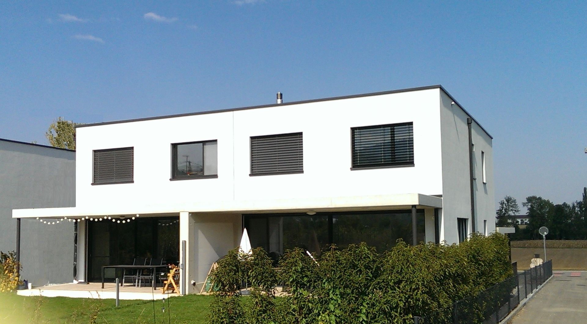 Modernes weißes Haus mit großen Fenstern, schwarzen Zierleisten und einer Terrasse.