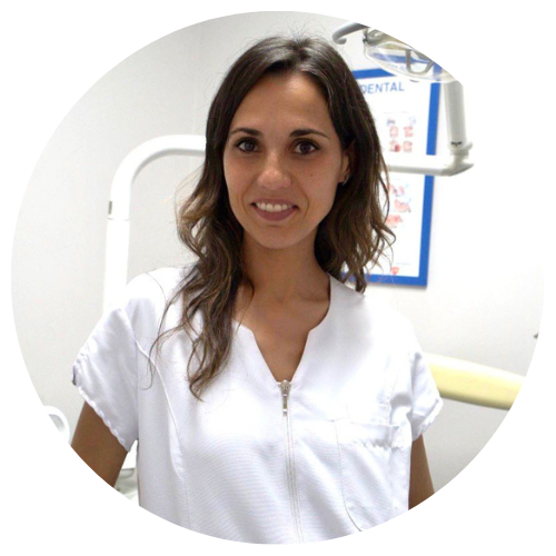 Una mujer con un uniforme blanco sonríe frente a un cartel que dice "dental".