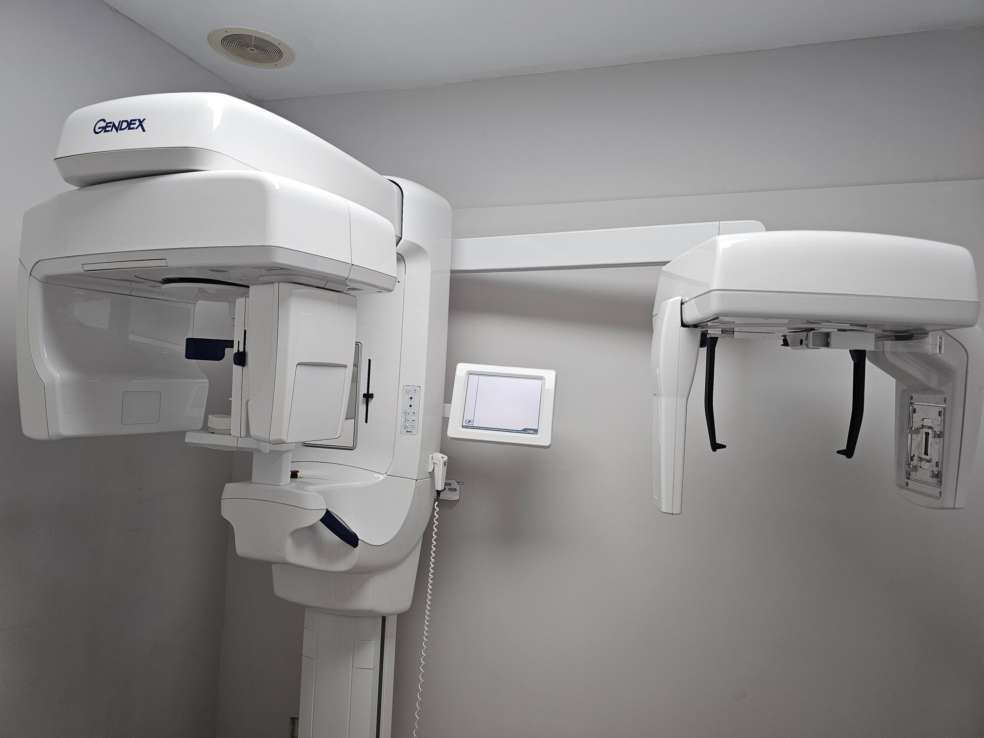 Sala de rayos X dental con equipo de imagen panorámica y controles montados en la pared en una sala de clínica blanca y limpia.