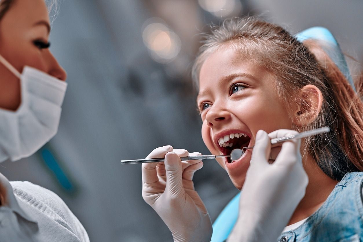 A una niña le están examinando los dientes un dentista.