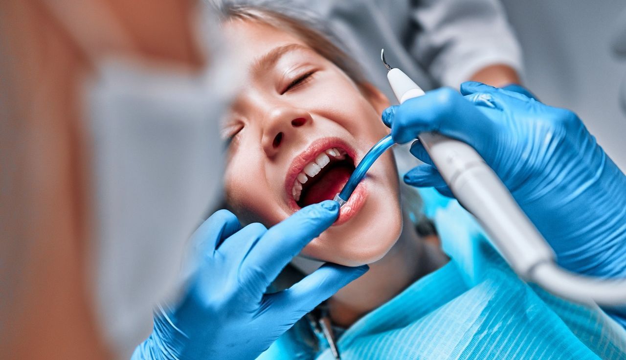 A una niña le están examinando los dientes un dentista.
