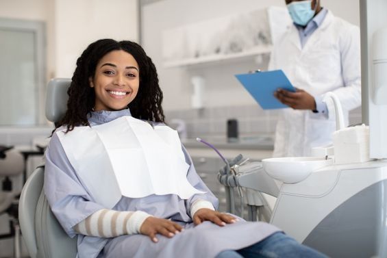 Una mujer está sentada en una silla dental sonriendo mientras un dentista la observa.