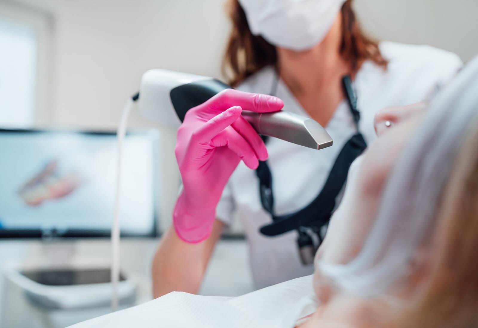 Un dentista con guantes rosas sostiene un instrumento dental cerca de un paciente en una clínica.