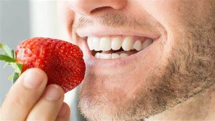 Un hombre está comiendo una fresa con la boca abierta.