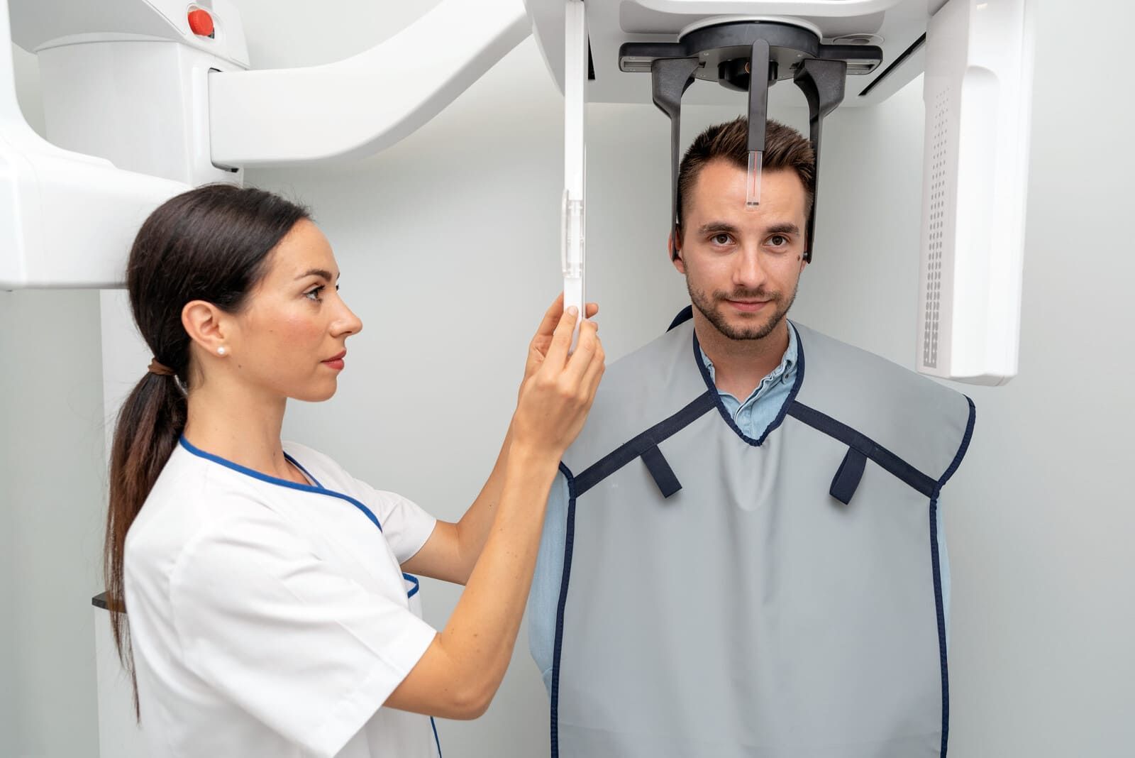 Un técnico ajusta una máquina de rayos X dental mientras un paciente lleva puesto un delantal protector de plomo.
