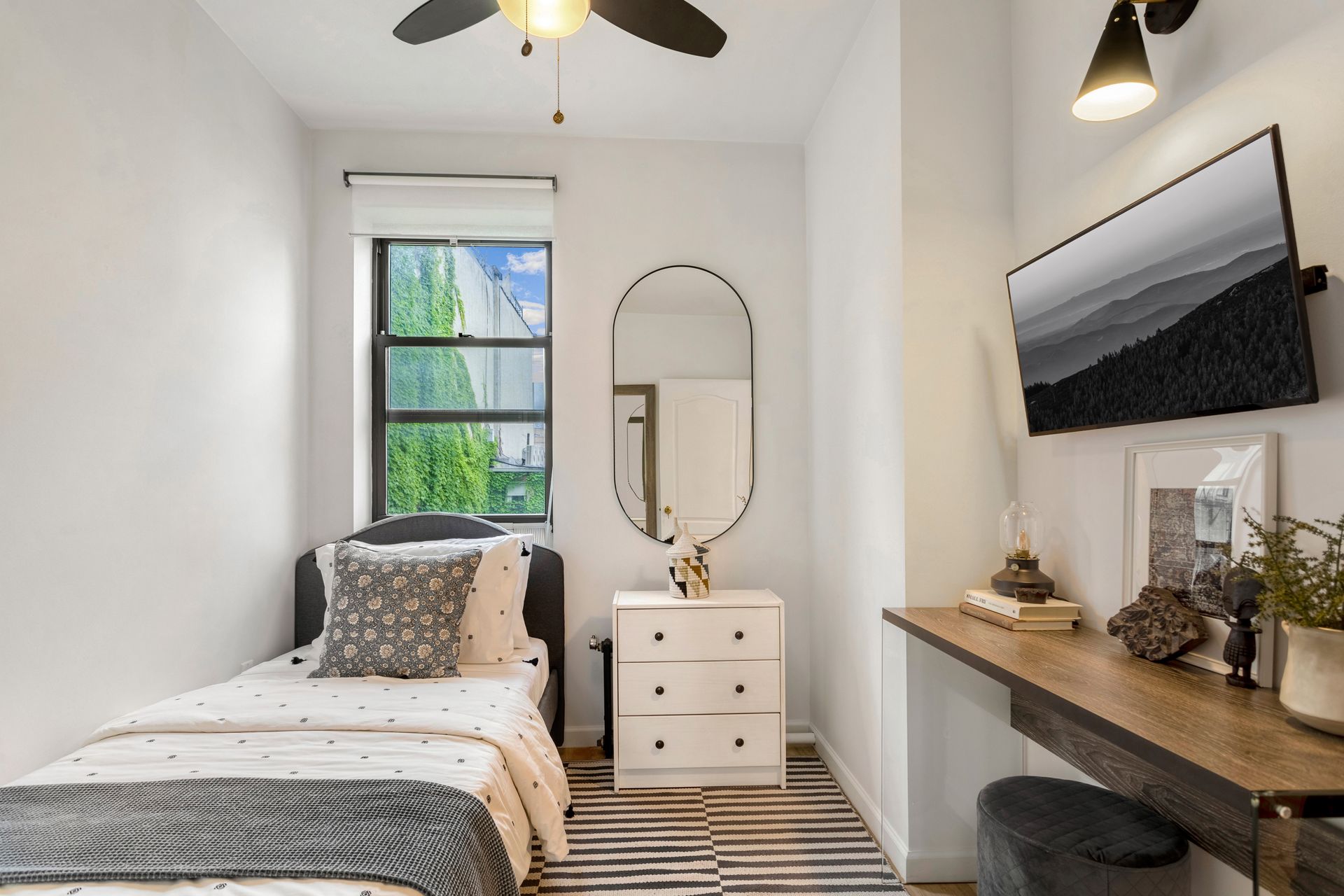 A bedroom with a bed , dresser , mirror and television.