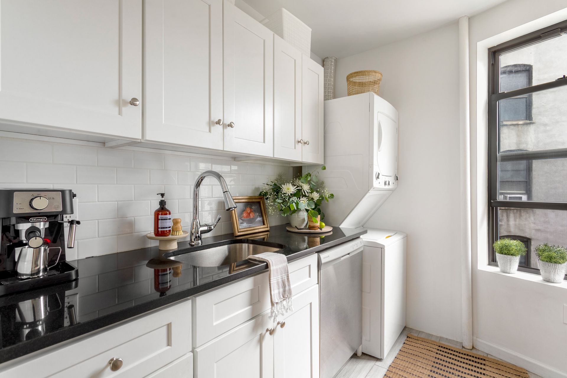 A kitchen with white cabinets , black counter tops , a sink and a window.