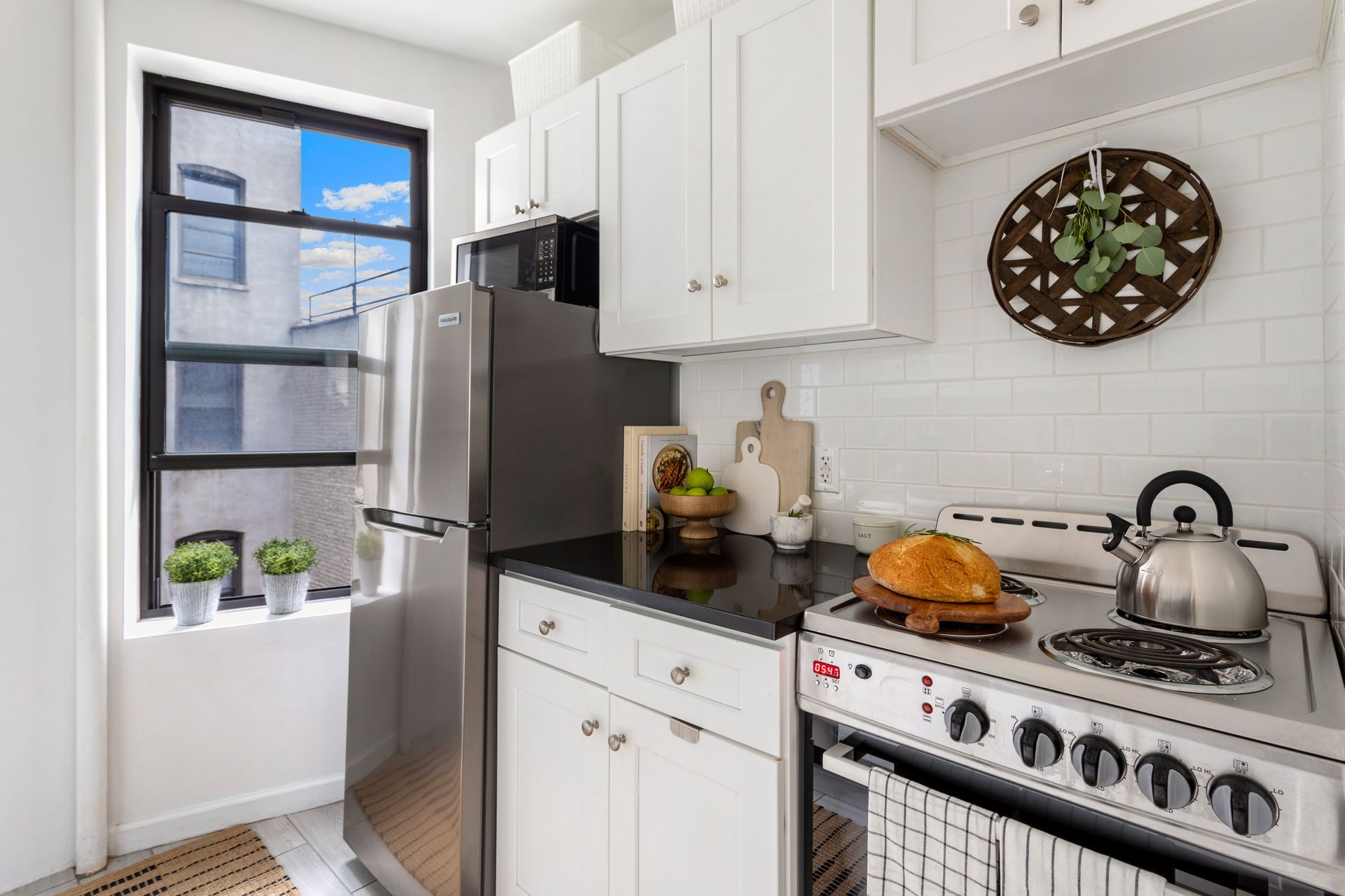 A kitchen with white cabinets , a stove , a refrigerator , and a window.