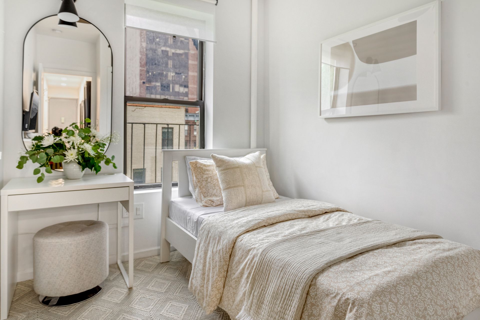 A bedroom with a single bed , dresser , mirror and ottoman.
