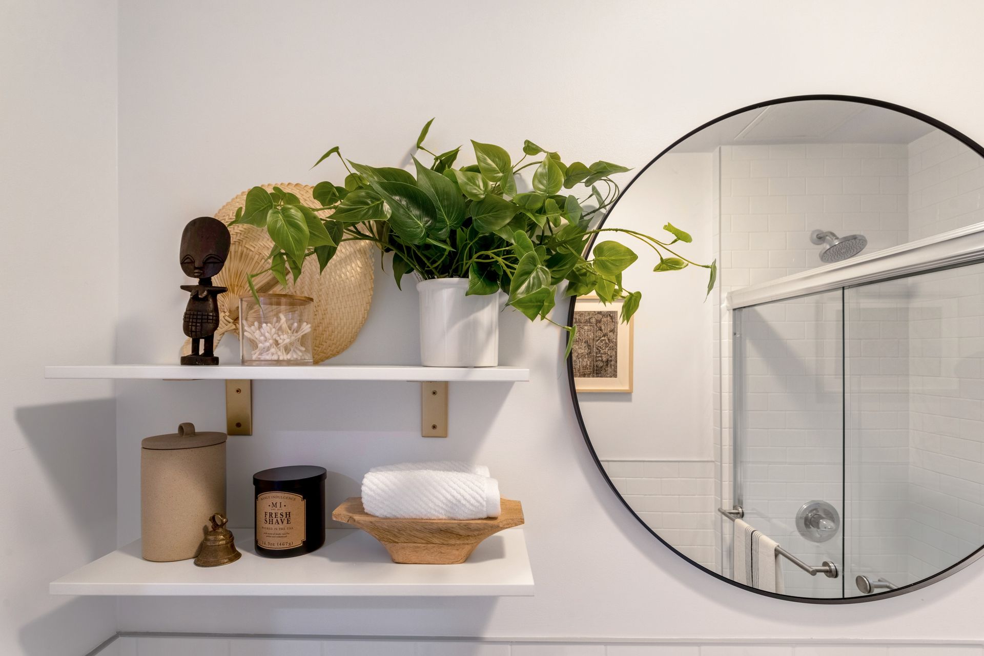 A bathroom with a round mirror and a plant on a shelf.
