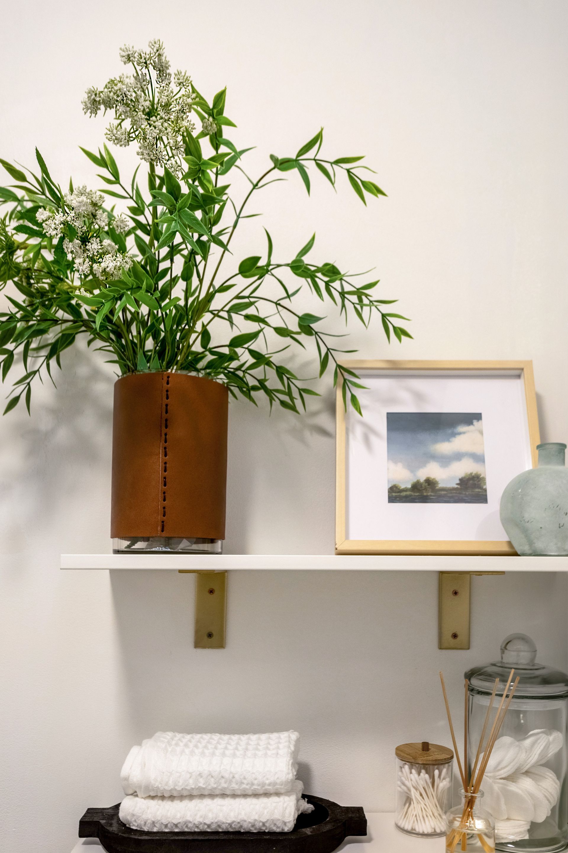 A bathroom shelf with a vase of flowers and a picture on it.