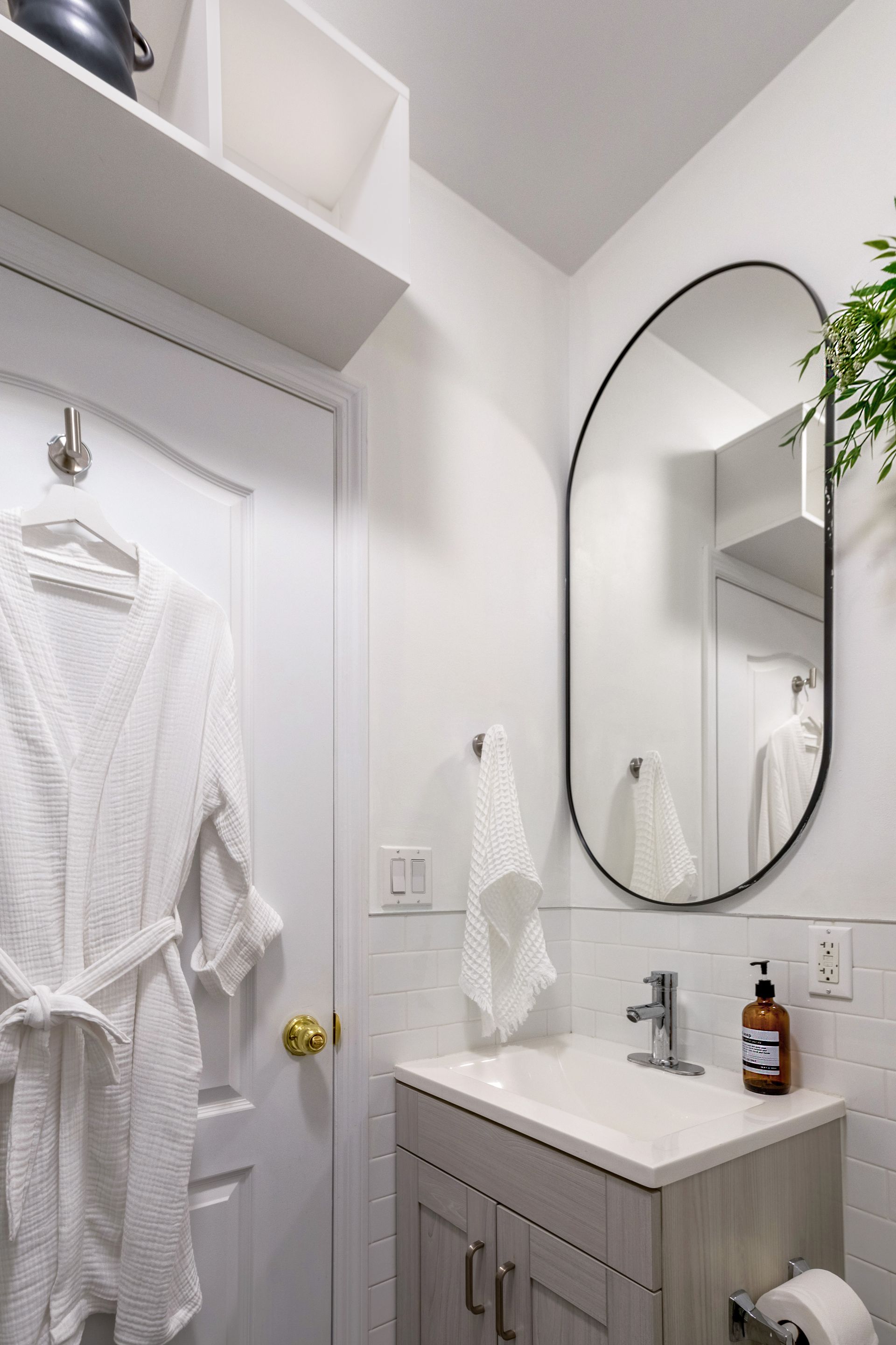 A bathroom with a sink , mirror and robe hanging on the door.