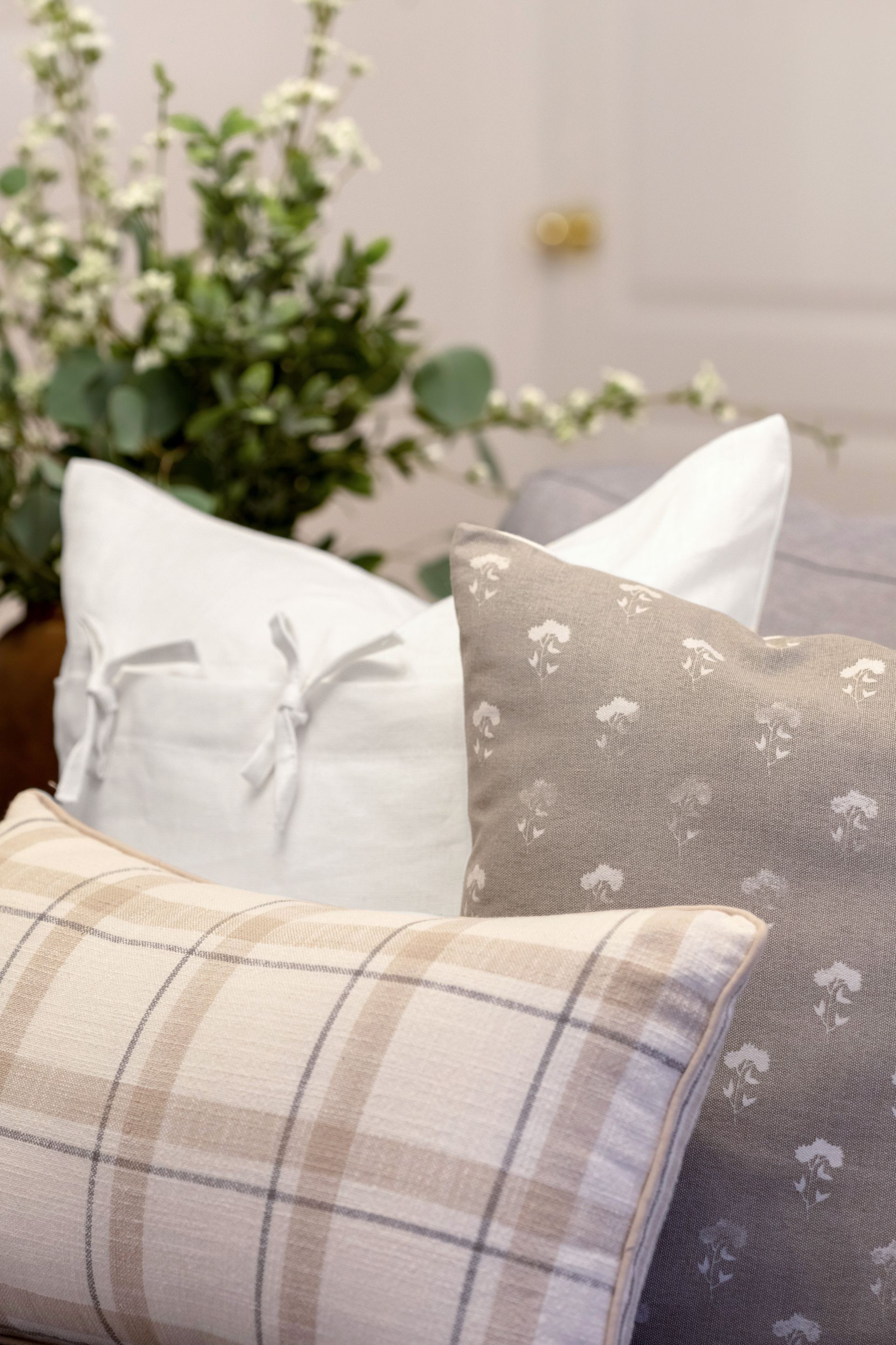A couch with three pillows on it and a plant in the background.