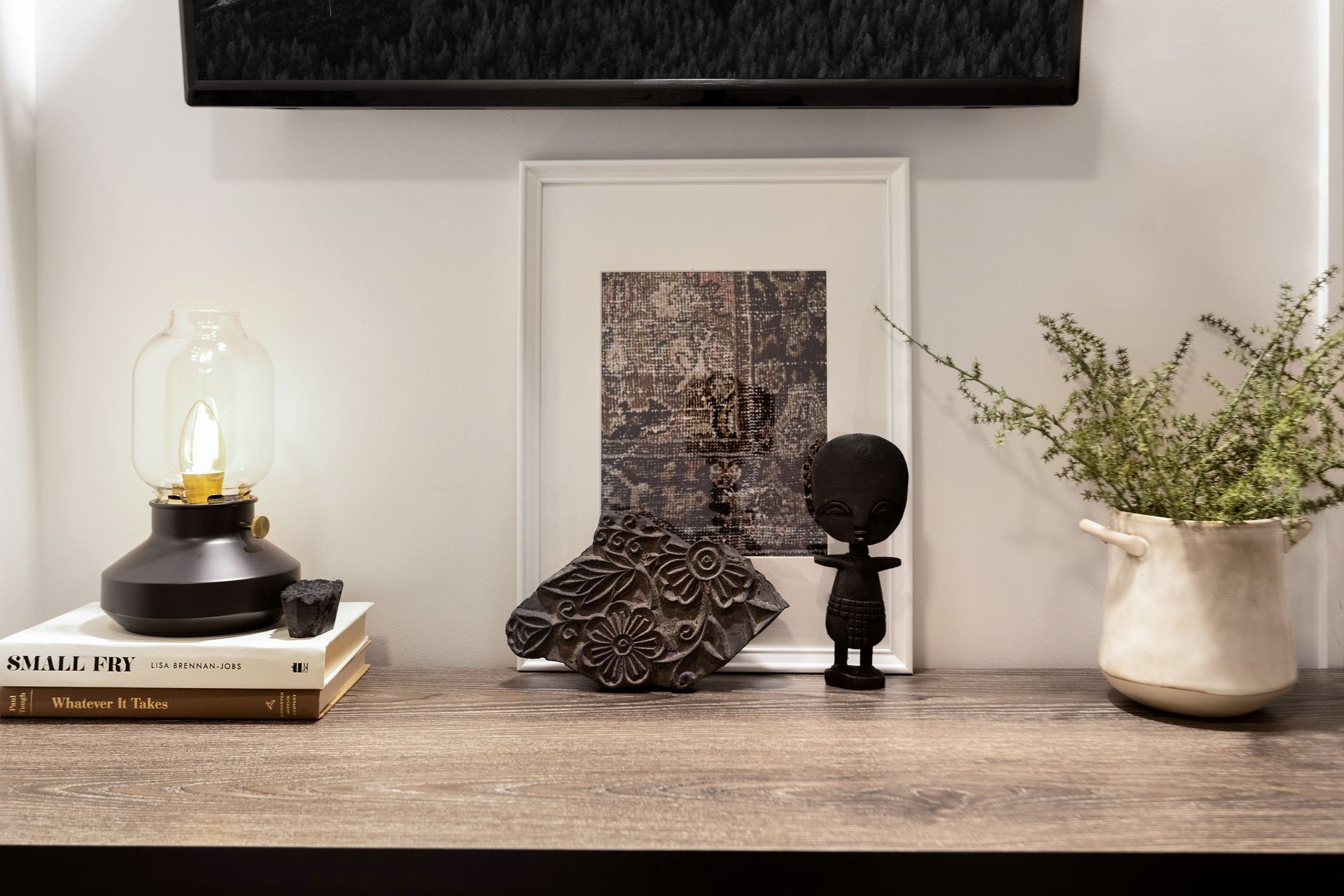 A wooden table with a picture on it , a lamp , a potted plant and a statue.
