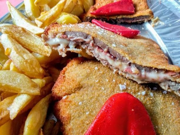 Plato de carne empanizada y frita con queso, pimiento rojo y patatas fritas.