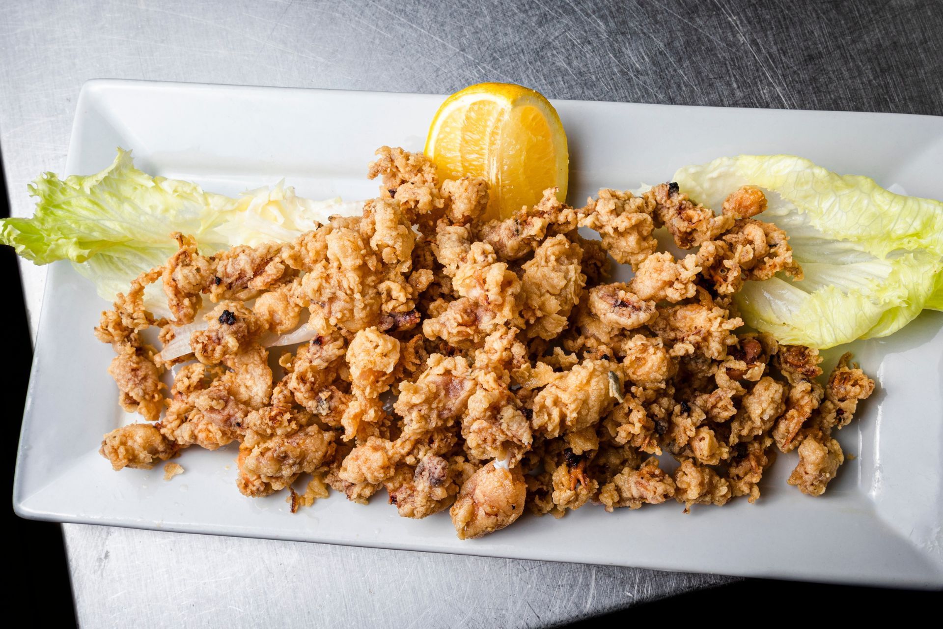 Calamares fritos con limón y lechuga en un plato rectangular blanco.