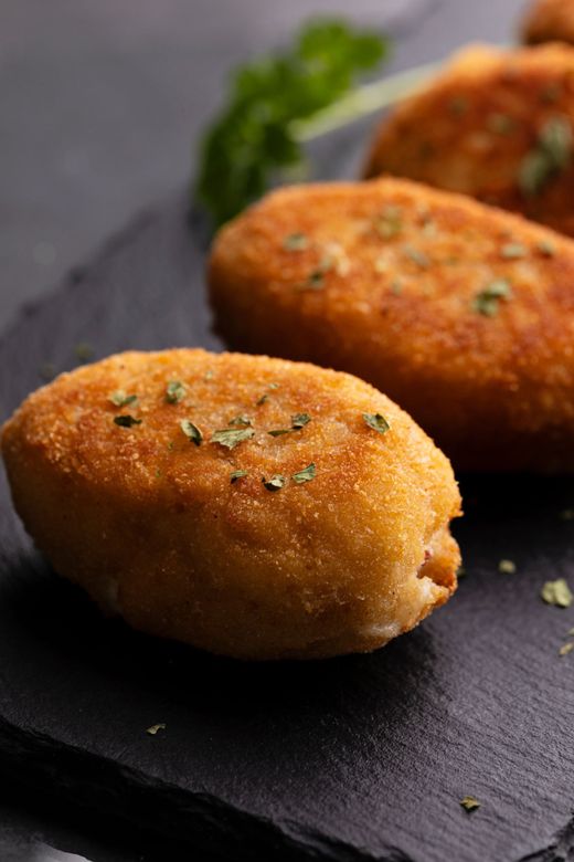 Croquetas doradas y fritas espolvoreadas con hierbas, dispuestas sobre una pizarra negra, primer plano.
