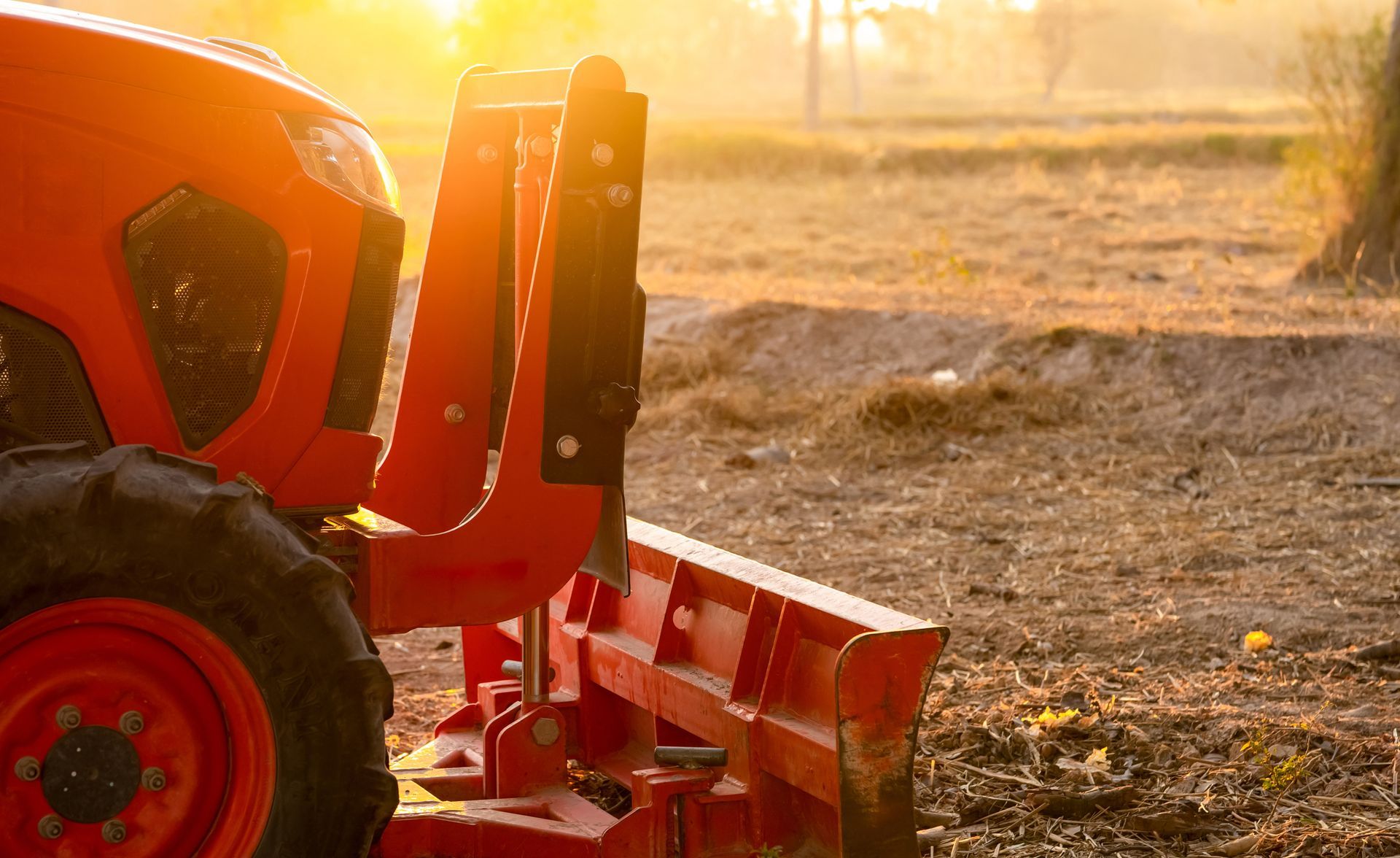 Oranger Traktor mit Frontlader auf einem sonnenbeschienenen Feld in der Abenddämmerung