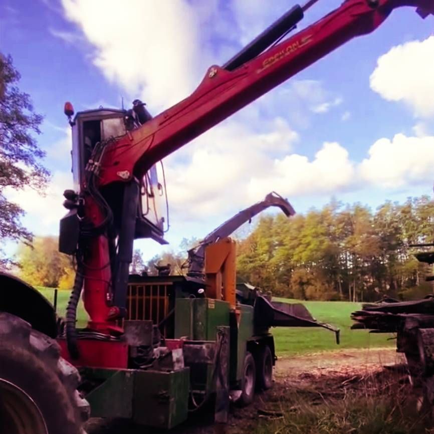 Zwei kleine rote Traktoren mit hellen Scheinwerfern parken nebeneinander auf einem nassen Industriegelände.