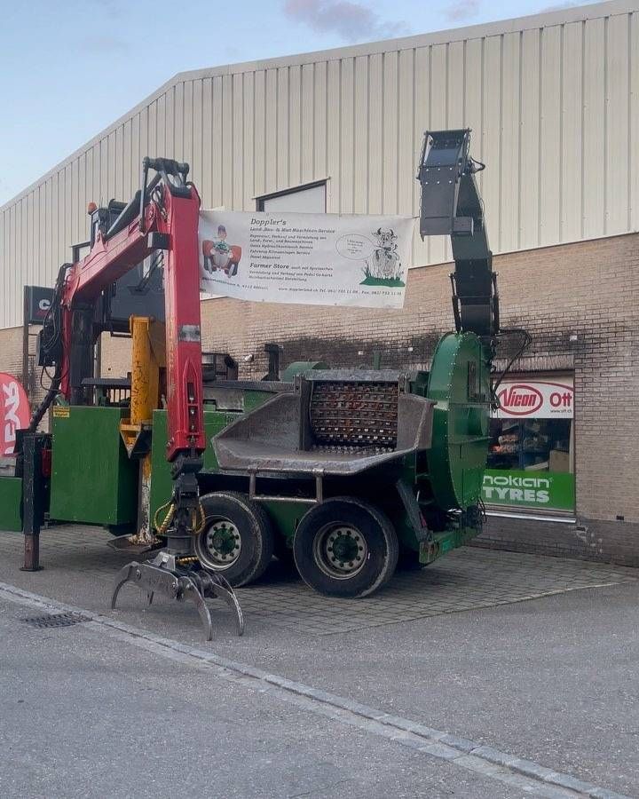 Ein roter und grüner Baustellen-Lkw mit Hebearm parkt im Freien neben einem Gebäude.
