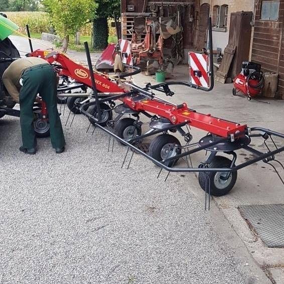 Roter Wartungswagen mit langem schwarzem Rahmen in einer Werkstatt; eine Person beugt sich über ein Rad auf der linken Seite.
