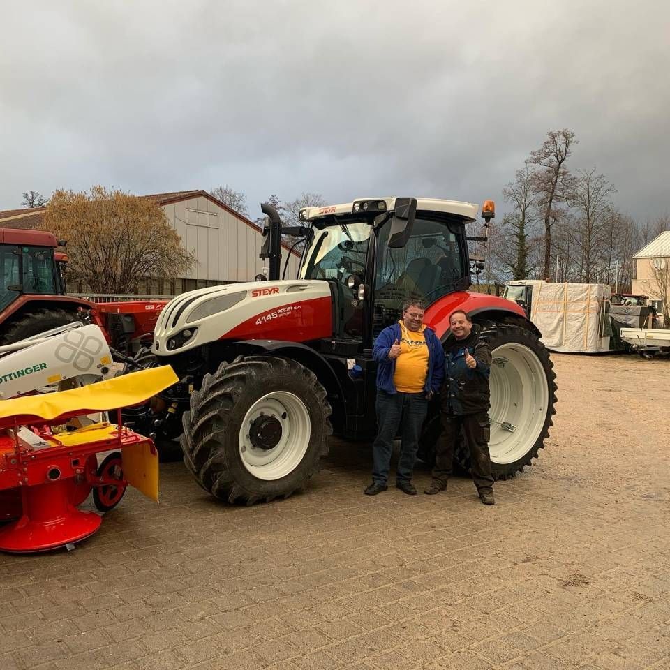 Zwei Personen stehen neben einem rot-weissen Traktor auf einem Freigelände.
