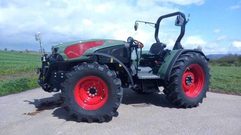 Grüner und roter Traktor, geparkt in einer Werkstatt oder auf einem Hof, Ansicht von vorne links