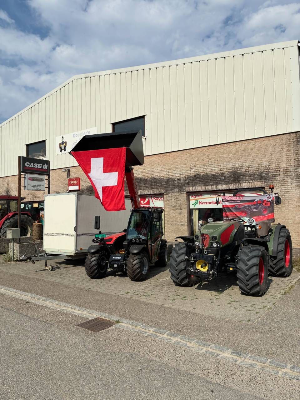 Drei Traktoren parkten vor einem Gebäude, über ihnen hing eine grosse rote Schweizer Flagge.